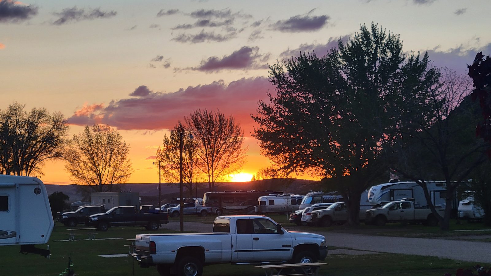 Sunset over Sunny Ridge RV Park — the high-desert sky glowing orange behind the RVs and trees