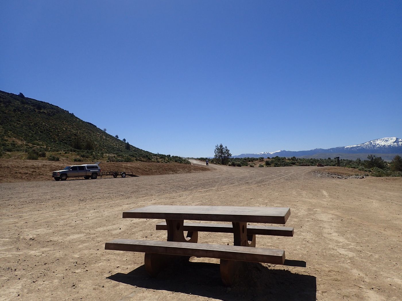 A gravel staging area and trailhead in high-desert OHV country with mountains beyond
