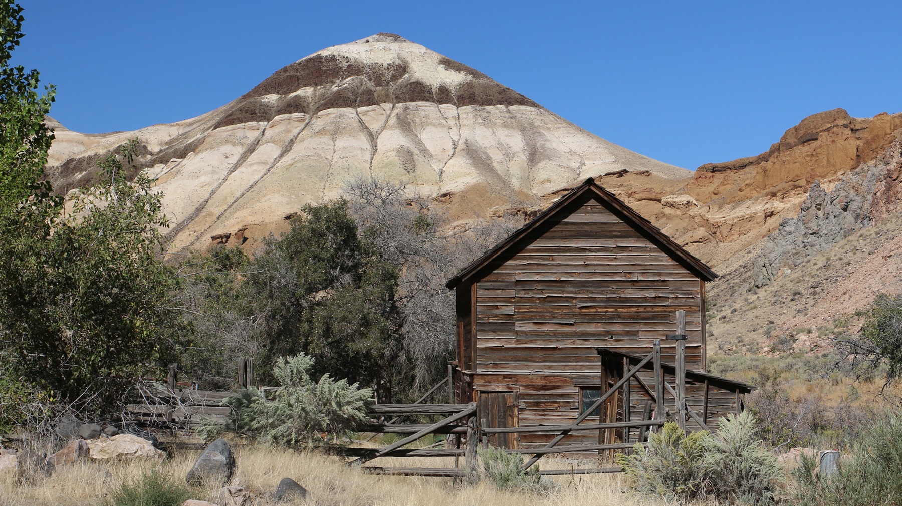 A green meadow framed by a dark lava-rock wall and wooden fence, with red canyon cliffs rising behind at Birch Creek