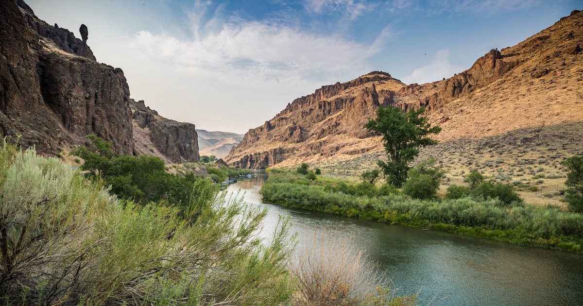 The Owyhee River curving through tall canyon walls below Owyhee Dam, with rafts on the water