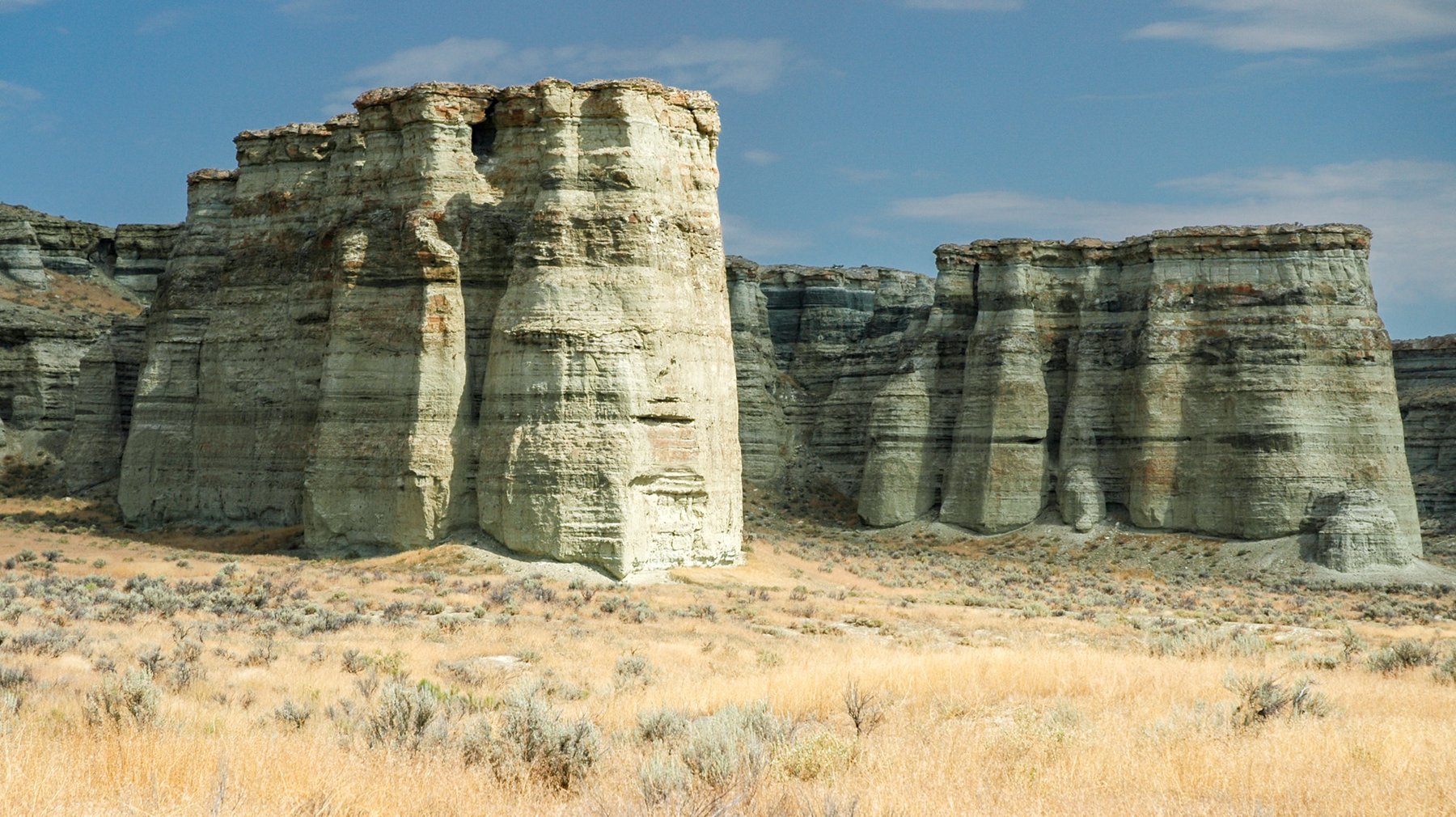 Close-up of the weathered, layered clay columns of the Pillars of Rome, with desert grass at their base